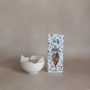 Pakke med blomsterdesign og vindue, ved siden af skål med flødekarameller pakket i papir.